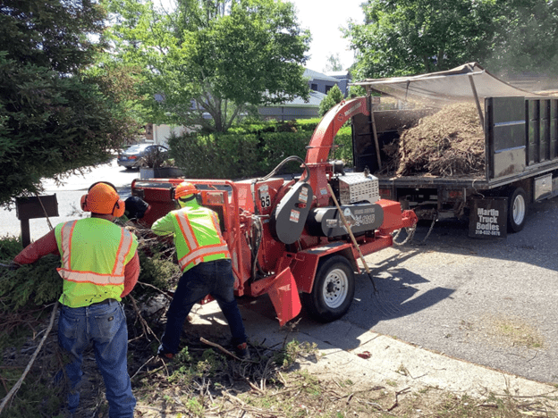 two people putting branches into a chipper machine.
