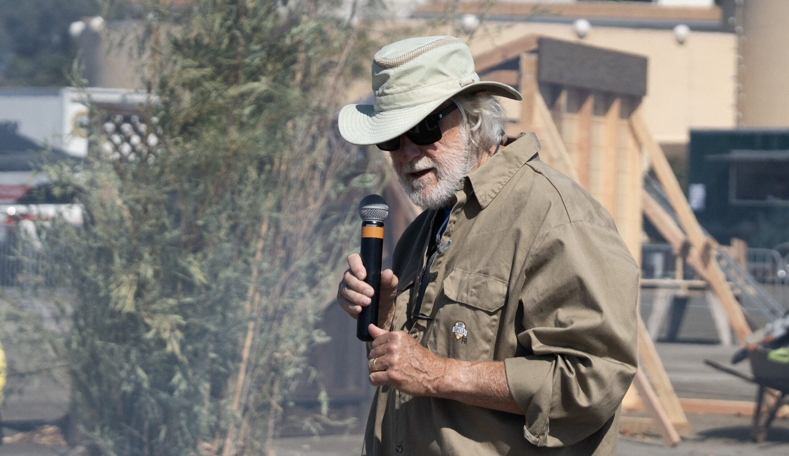 Dr. Steve Quarles wearing a tan fishing hat and sunglasses, holding a microphone up to his mouth.