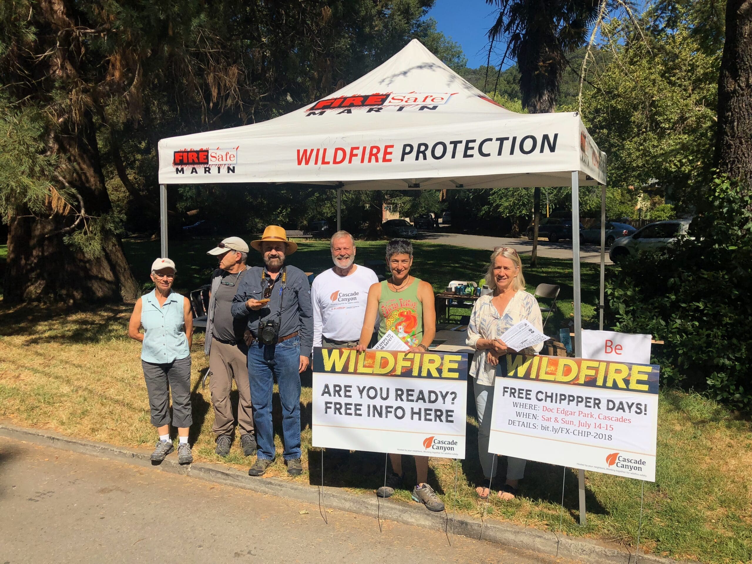 People staffing an information tent at a park. The information on display is related to wildfire safety.