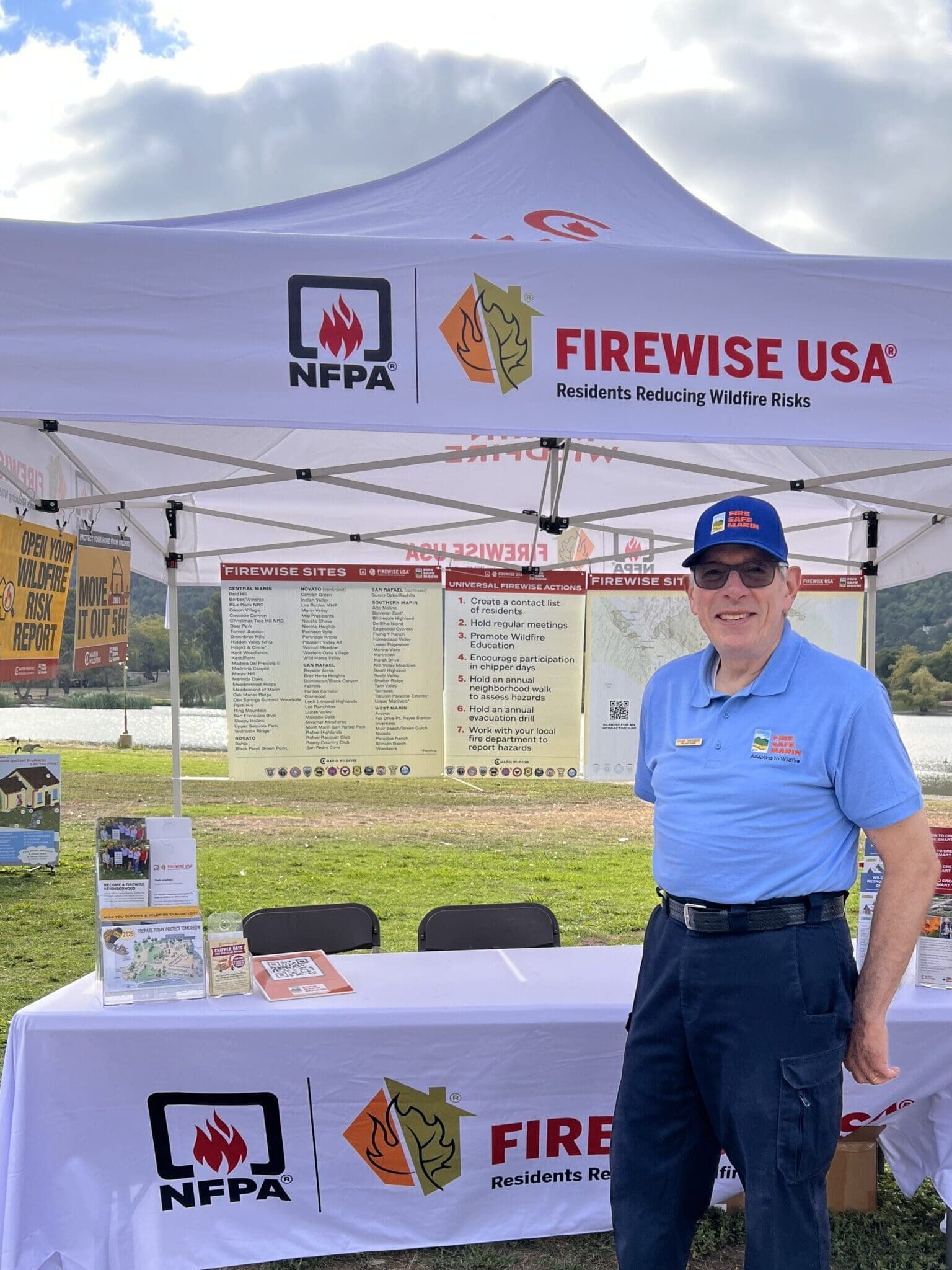 A gentleman in a Fire Safe Marin polo standing in a tent with safety tips on posterboard hung up behind him.