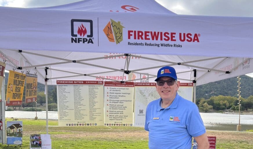 Stu Tanenberg in a Fire Safe Marin polo standing in a tent with safety tips on posterboard hung up behind him.