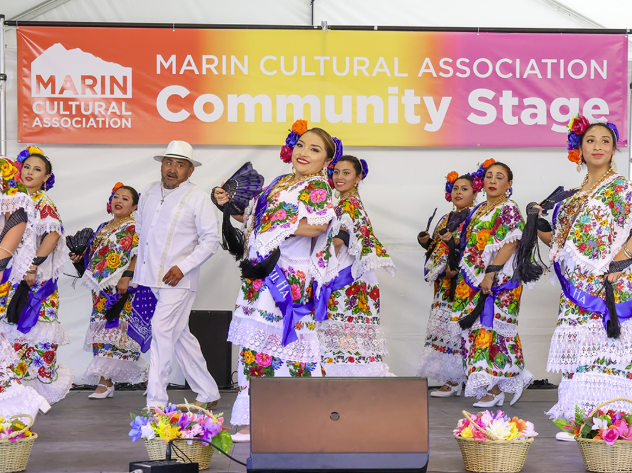 Dancers performing on a stage in front of a banner that reads "Marin Cultural Association: Community Stage".