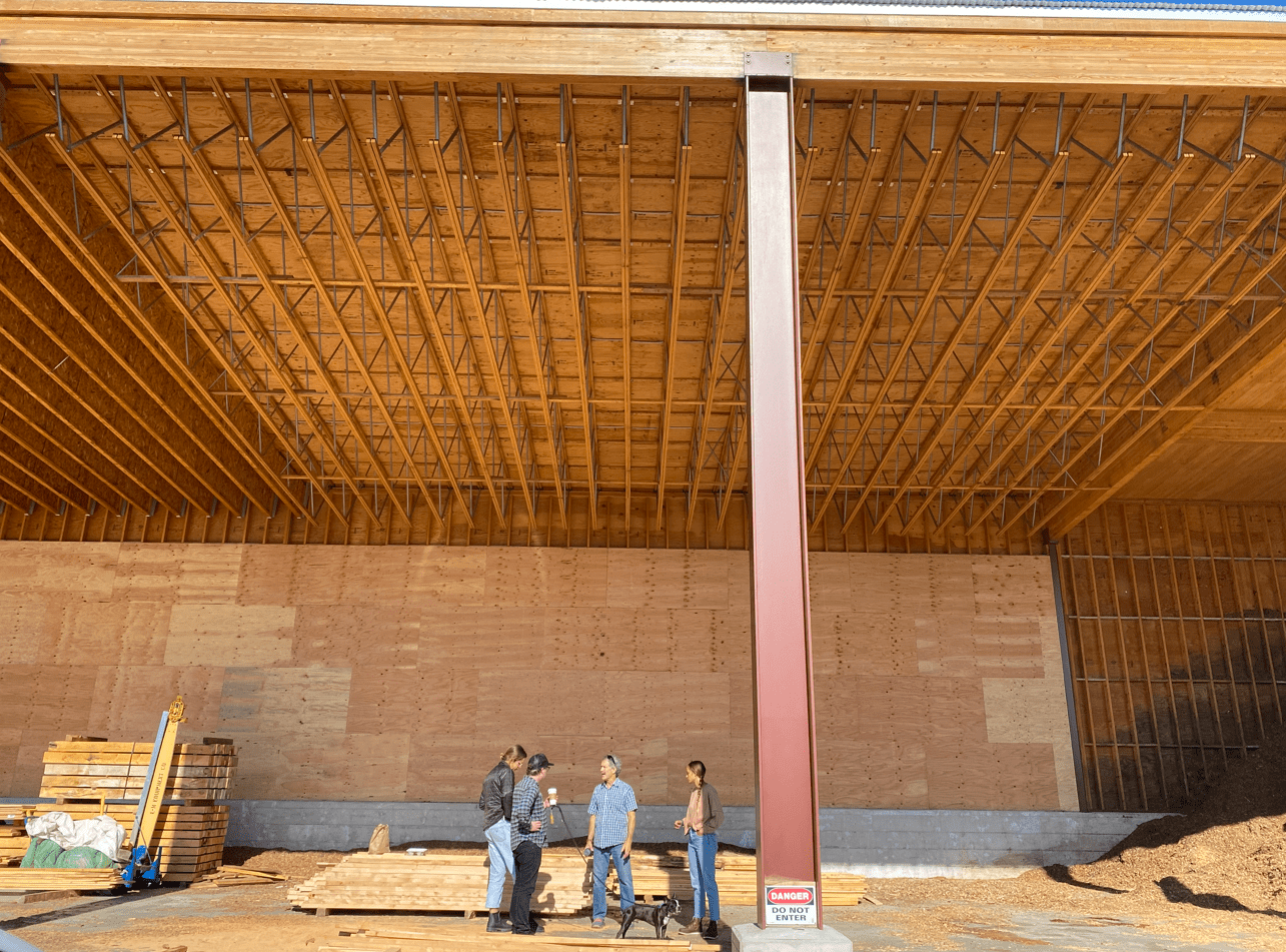 Four people standing, talking in a very large room made of primarily wood.